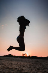 Girl jumping on sand at sunset