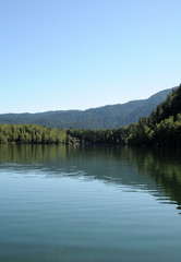 In the clear water of a forest lake reflects the sky, mountain, forest and clouds. Photo partially tinted. 