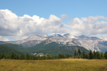 Obraz premium Blue sky and cumulus clouds over the Eastern Sayan Mountains and Mount MunKu-Sardyk. Photo partially tinted.