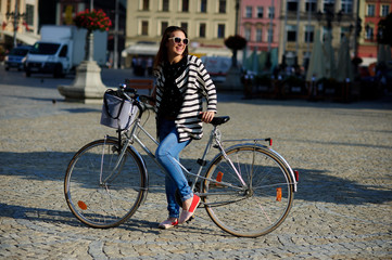 Fototapeta na wymiar Cute young brunette in sunglasses with bicycle on a paved pavement.
