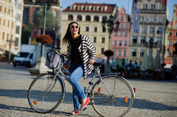 Fototapeta na wymiar Cute girl in a striped cardigan with bicycle on the street of the ancient city. Sunny warm day.