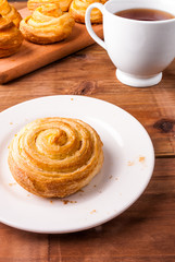Freshly baked cinnamon rolls. In the foreground a bun on a plate, a mug of tea is near