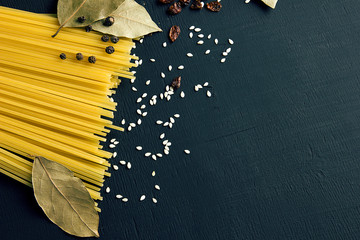 Raw spaghetti and Bay leaf, barberry, pepper, sesame seeds on black-blue wooden background, top view place for text