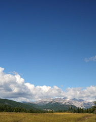 Blue sky and cumulus clouds over the Eastern Sayan Mountains and Mount MunKu-Sardyk. Photo partially tinted.