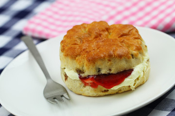 Traditional scone with raisins  with clotted cream and jam on white plate
