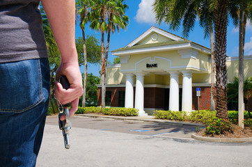 A criminal with a pistol gun is standing outside of a bank as he prepares to commit bank robbery and rob them of large amounts of money.