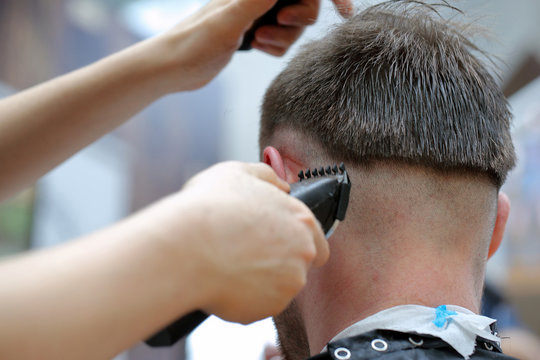 Hairdresser coiffeur makes hairstyle with electric trimmer and c