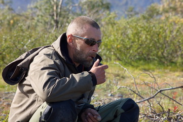 Bearded man in a waterproof suit and sunglasses smokes a pipe on a halt.