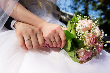 Obraz na płótnie Canvas Bride and groom hands with wedding rings holding pink roses bouquet