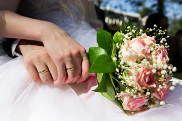 Obraz na płótnie Canvas Bride and groom hands with wedding rings holding pink roses bouquet