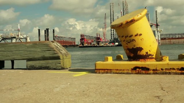 Camera dollies past maritime bollards on a dock to show drilling platforms in a harbor.