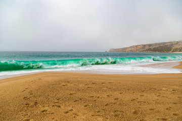 Crushing emerald waves on sandy beach in Nazare, Portugal