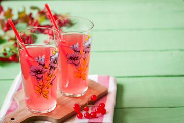 Fresh viburnum drink in glass on green wooden background with leaves and berries. Selective focus.