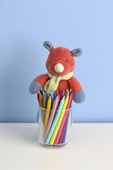 glass with colorful crayons and a soft toy