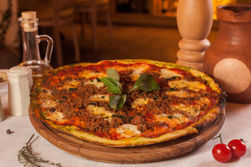 Pizza with meat and basil on a wooden tray