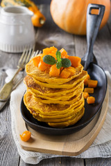 Pumpkin pancakes with mint leaves and sauce on the old wooden background. Rustic style. Selective focus.