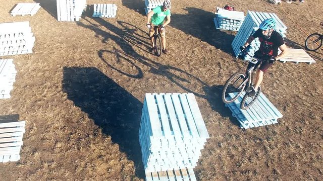 Two cyclists doing jump MTB tricks in bicycle 4k aerial video. Mountain bike trial rider in pallet park. Extreme sport lifestyle