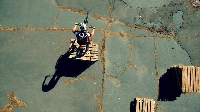 Сyclist doing jump MTB tricks in bicycle 4k top view aerial video. Mountain bike trial rider in box park. Extreme sport lifestyle