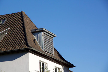 House with dormer windows and closed shutters against a blue sky