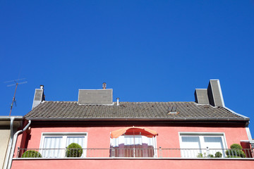 Red house with sunshade on balcony and chimney on roof against a blue sky in Aachen, Germany