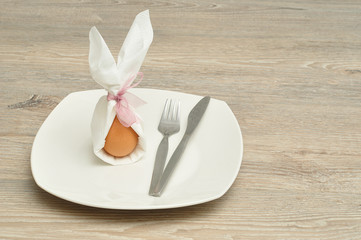 An egg in a napkin with bunny ears displayed on a plate 