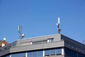 Fototapeta premium Exterior view of the upper floor and roof of a modern flat roof urban house with communication antennae on the rooftop against a blue sky
