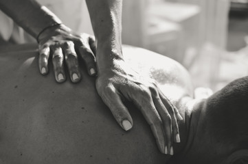 Black and white close-up on female masseur hands on man back during a session, sun light background