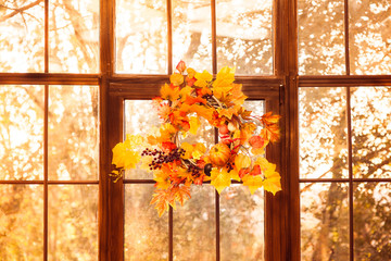 Autumn wreath entwined with leaves, garlic, berries, pumpkins, mushroom, hanging on the wooden window.