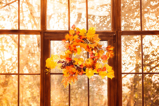 Autumn wreath entwined with leaves, garlic, berries, pumpkins, mushroom, hanging on the wooden window.