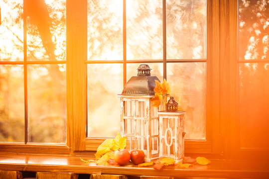 Vintage lanterns, autumn leaves, red ripe apples at wooden windowsill in the lights of sunset.