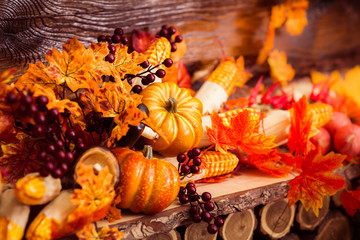 Autumn still life with marple leaves, vinous berries and october vegetables at the dark wooden background.
