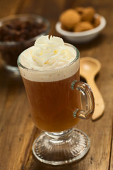 Fresh hot chocolate herbal tea made of cacao shell flakes in glass with whipped cream on top on dark wood  (Selective Focus, Focus on the front of the cream)
