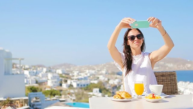 Woman taking photo of breakfast using mobile smart phone. Girl taking pictures of food on luxury travel vacation for social media. Beautiful female in resort in Mykonos, Greece, Europe.