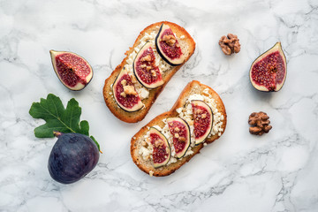 Crusty toast with figs fruits, goat cheese, honey and walnut on marble table. Top view