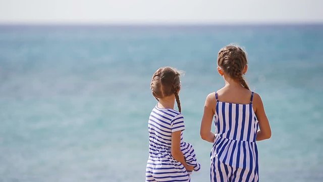 Adorable little girls together throw stones during beach vacation. Kids enjoy summer vacation in greek beach