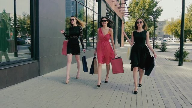 Group of attractive young women walking along shop windows. Slow motion