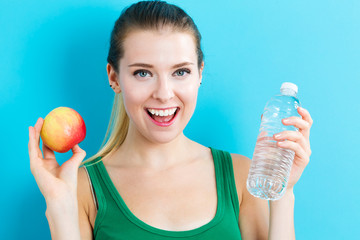 Happy young woman holding apple and water