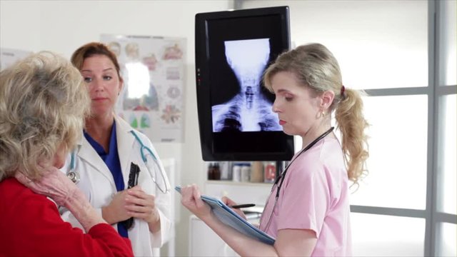 A doctor and her nurse discuss with an elderly patient the x-rays displayed on a monitor.