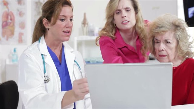 A pretty doctor uses a laptop to show a course of patient care with an elderly woman and her daughter.