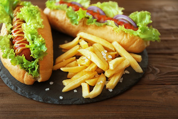 Delicious hot dog and fries on round wooden board