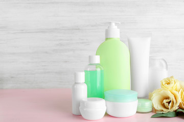 Different cosmetic bottles and flowers on grey wall background