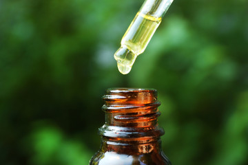 Mint oil dripping into bottle on blurred natural background