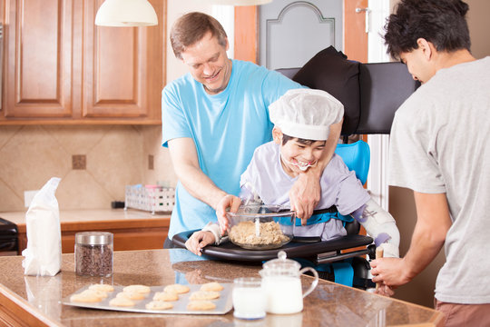 Disabled boy in stander baking cookies with father and brother - Powered by Adobe