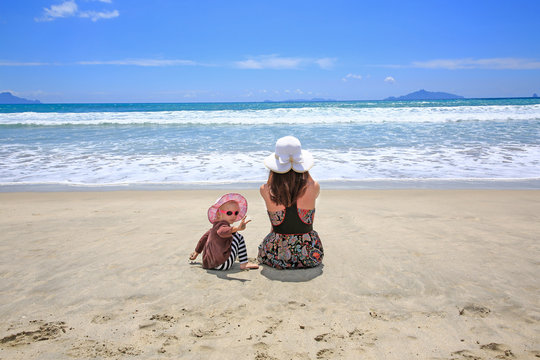 Young pretty woman with little daughter sitting on Sandy Beach