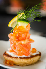 One Blini appetizer with smoked salmon and sour cream, garnished