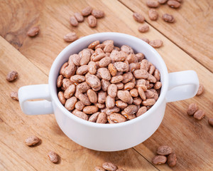 Close up Brown pinto beans in white bowl on wooden background. S