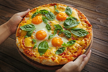 Margarita pizza with basil leaves and egg in female hands on wooden background