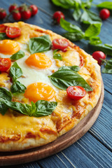 Margarita pizza with basil leaves and egg on wooden table closeup