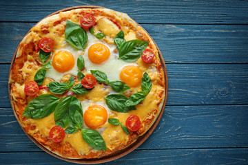 Margarita pizza with basil leaves and egg on wooden table, top view
