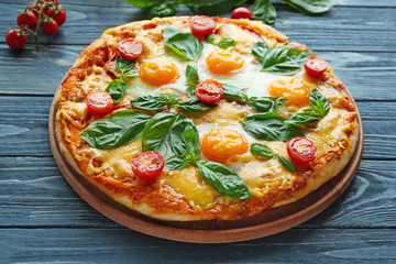 Margarita pizza with basil leaves and egg on wooden table closeup